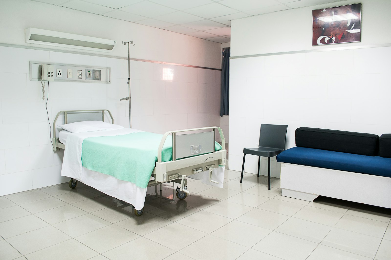An empty hospital room with a bed and a visitor sofa